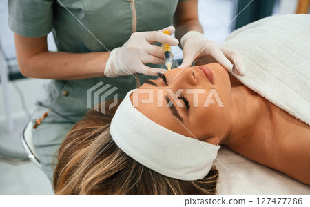 Injection into the face skin. Woman face getting facial care by beautician hands at spa salon Injection into the face skin. Woman face getting facial care by beautician hands at spa salon 127477286