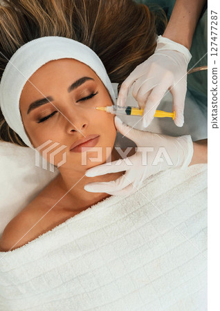 Injection into the face skin. Woman face getting facial care by beautician hands at spa salon Injection into the face skin. Woman face getting facial care by beautician hands at spa salon 127477287