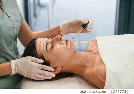Putting liquid on lips. Woman face getting facial care by beautician hands at spa salon Putting liquid on lips. Woman face getting facial care by beautician hands at spa salon 127477304