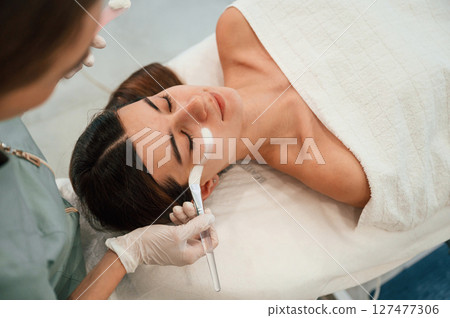 Facial mask. Woman is taking care off customer by beautician hands at spa salon Facial mask. Woman is taking care off customer by beautician hands at spa salon 127477306