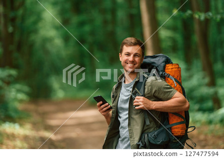 Big backpack and smartphone. Tourist in summer forest. Conception of exploration and leisure Big backpack and smartphone. Tourist in summer forest. Conception of exploration and leisure 127477594