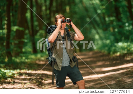 Looking through the binoculars. Tourist in summer forest. Conception of exploration and leisure 127477614