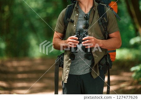 Holds binoculars. Close up view of tourist that is in summer forest 127477626
