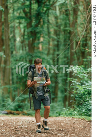 Walking forward with map in hands. Tourist in summer forest. Conception of exploration and leisure 127477633