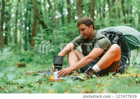 Boiling water, sitting near the tent. Tourist in summer forest. Conception of exploration and leisure Boiling water, sitting near the tent. Tourist in summer forest. Conception of exploration and leisure 127477639