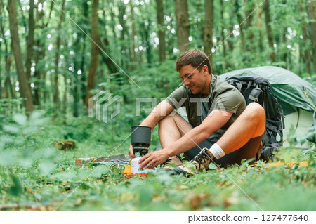 Sitting near the tent. Tourist in summer forest. Conception of exploration and leisure Sitting near the tent. Tourist in summer forest. Conception of exploration and leisure 127477640