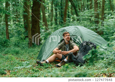 With cup of water. Sitting near the tent. Tourist in summer forest. Conception of exploration and leisure With cup of water. Sitting near the tent. Tourist in summer forest. Conception of exploration and leisure 127477648