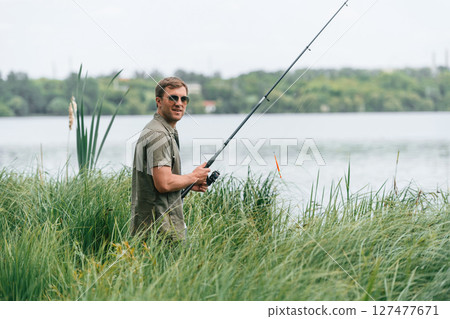 Positive and handsome man in sunglasses is fishing outdoors Positive and handsome man in sunglasses is fishing outdoors 127477671