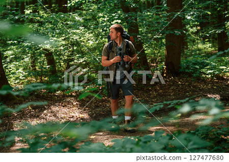 Looking for the way. Holding binoculars. Tourist in summer forest. Conception of exploration and leisure 127477680