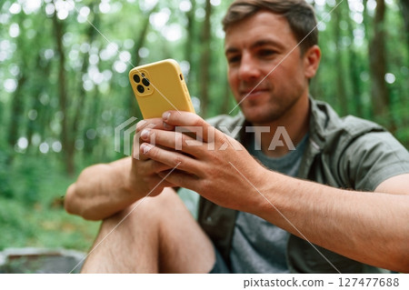 Using yellow colored smartphone. Tourist in summer forest. Conception of exploration and leisure 127477688