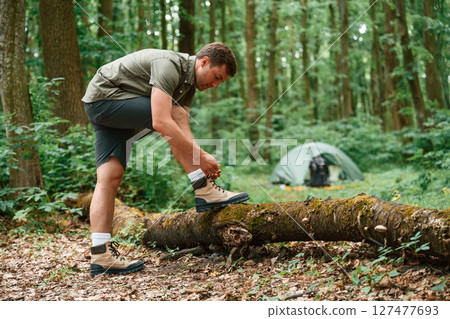 Standing and ties shoelaces. Tourist in summer forest. Conception of exploration and leisure 127477693