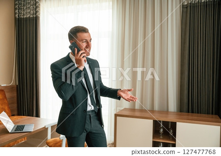 Talking by phone. Businessman is indoors in the hotel room 127477768