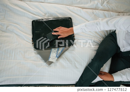 Close up view of businessman that is sitting on bed with tickets for travel on it Close up view of businessman that is sitting on bed with tickets for travel on it 127477812
