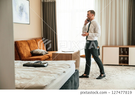 Phone conversation. Businessman is indoors in the hotel room Phone conversation. Businessman is indoors in the hotel room 127477819