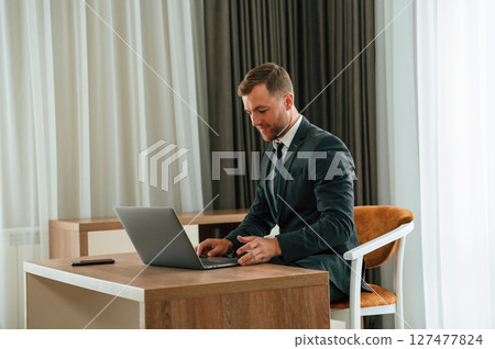 In the office with laptop. Handsome businessman is indoors in the hotel room 127477824