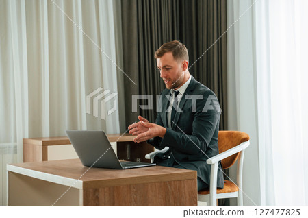 In the office with laptop. Handsome businessman is indoors in the hotel room In the office with laptop. Handsome businessman is indoors in the hotel room 127477825