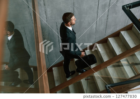 Walking up. Man in business suit and tie with case in hands is on the stairs 127477830