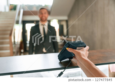 Making payment by using phone and terminal. A man in a black jacket at the hotel reception Making payment by using phone and terminal. A man in a black jacket at the hotel reception 127477845