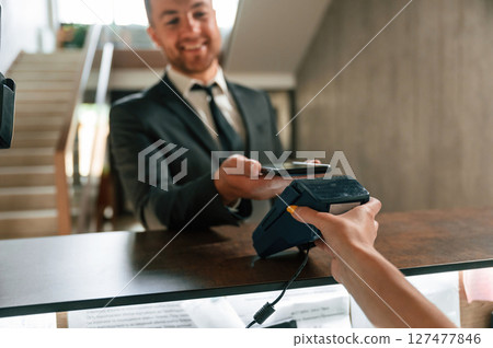 Wireless payment by using phone and terminal. A man in a black jacket at the hotel reception 127477846