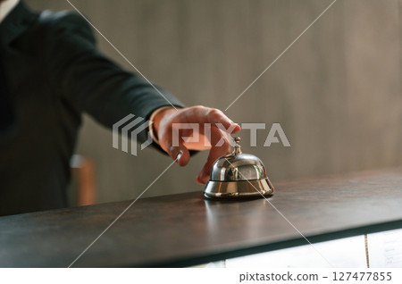 Close up view, using hotel desk bell. A man in a black jacket at the hotel reception Close up view, using hotel desk bell. A man in a black jacket at the hotel reception 127477855