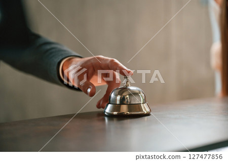 Close up view, using hotel desk bell. A man in a black jacket at the hotel reception Close up view, using hotel desk bell. A man in a black jacket at the hotel reception 127477856