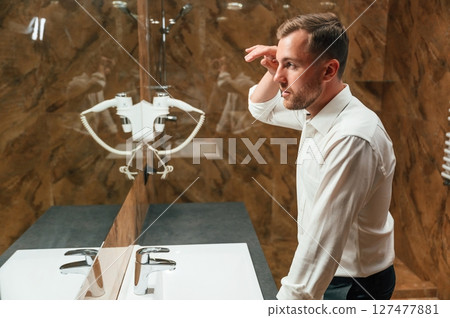 Man in formal clothes is in the bathroom against mirror Man in formal clothes is in the bathroom against mirror 127477881