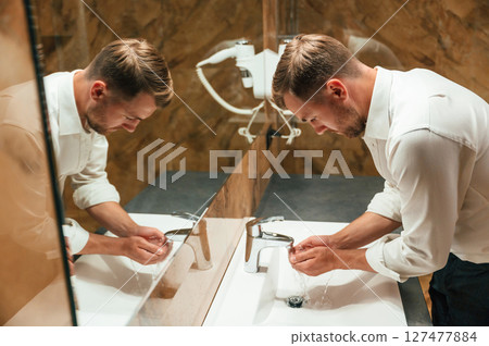 Washing hands. Man in formal clothes is in the bathroom against mirror Washing hands. Man in formal clothes is in the bathroom against mirror 127477884