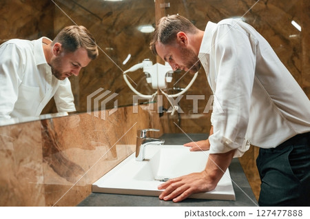 Man in formal clothes is in the bathroom against mirror 127477888
