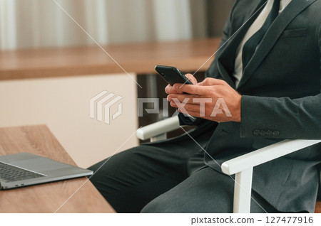 Close up view of businessman that is sitting and using smartphone Close up view of businessman that is sitting and using smartphone 127477916