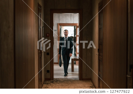 Front view, in the appartment. Handsome businessman is indoors in the hotel room Front view, in the appartment. Handsome businessman is indoors in the hotel room 127477922