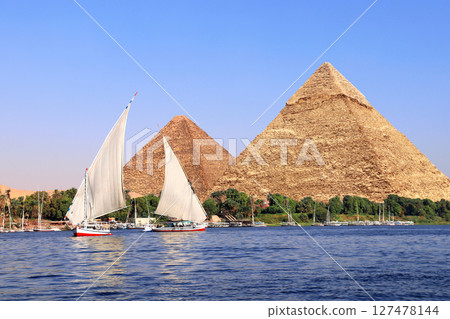 Great Pyramids of Chephren and Cheops and traditional sailing boat felucca, Nile river, Egypt. Famous tourist attraction sailing boat ride. Topic of travel, trip abroad on vacation, cruises and tours 127478144