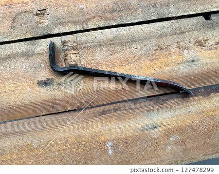 Close up of crowbar lying on rough wooden surface, highlighting texture and tools used in manual labor, carpentry or construction work 127478299