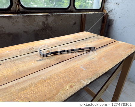 Rusty pry bar lying on a rough wooden workbench in a partially renovated room. The old peeling wall and dusty windows add a gritty, authentic construction site atmosphere 127478301