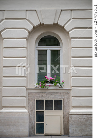 Elegant arched window with pink flowers on classic beige building facade Elegant arched window with pink flowers on classic beige building facade 127478511