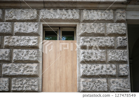 Wooden board covering lower window part on textured stone building facade 127478549