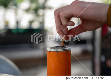 hand pressing cigarette butt against an orange public ashtray pole, concept of anti-littering 127478589