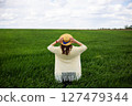 A woman in a straw hat stands in a vast green field, enjoying the peaceful countryside view 127479344