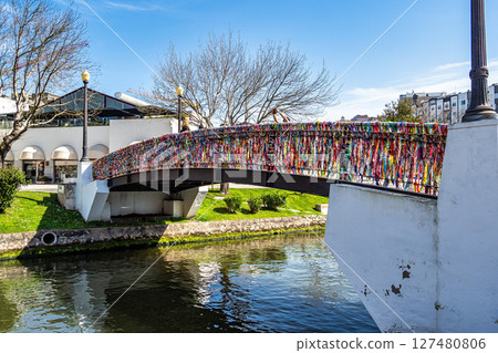 Moliceiro boats sails along the canal toward the Love Lock Bridge decorated with colorful ribbons in Aveiro, Portugal Moliceiro boats sails along the canal toward the Love Lock Bridge decorated with colorful ribbons in Aveiro, Portugal 127480806