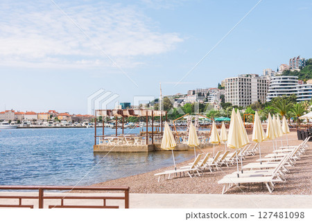 Empty sun loungers and closed umbrellas on the Adriatic coast. Summer beach infrastructure and seaside tourism in Budva, Montenegro 127481098