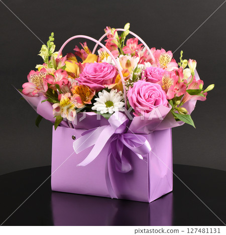 A bouquet and a violet bag with handles black background. Bouquet of flowers, chrysanthemum, rose, lily, carnation. 127481131