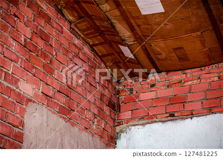 Unfinished red brick wall with visible wooden ceiling beams 127481225