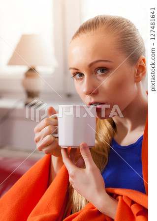 Woman lying on sofa under blanket drinking tea Woman lying on sofa under blanket drinking tea 127481641