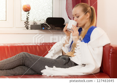 Woman lying on sofa under blanket drinking tea 127481645