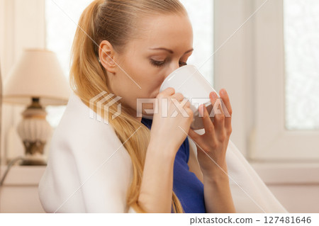 Woman lying on sofa under blanket drinking tea 127481646