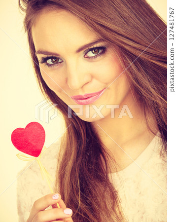 Flirty woman holding red wooden heart on stick 127481767