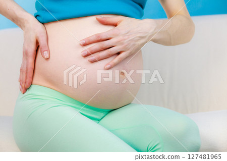 Pregnant woman sitting on couch holds hand on her back 127481965