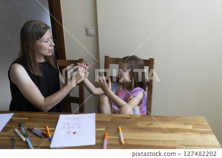 Teacher helping young girl learning sign language at home Teacher helping young girl learning sign language at home 127482202