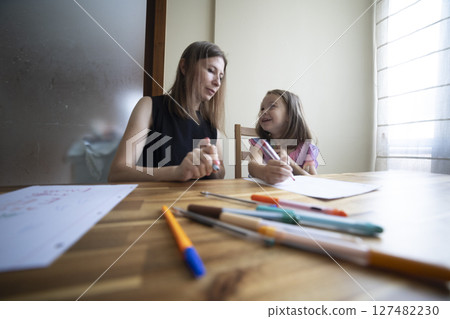 Mother helping daughter drawing with colored markers at home 127482230