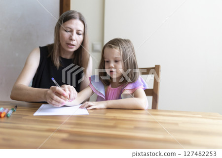 Teacher helping young girl writing on paper at desk Teacher helping young girl writing on paper at desk 127482253