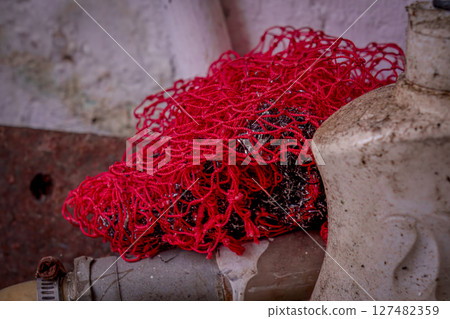 Tangled red netting discarded on a dirty pipe surface 127482359